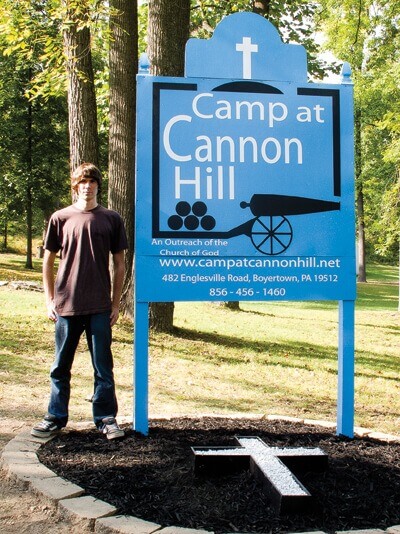 Ben Devan stands next to the new sign at Camp Cannon Hill.