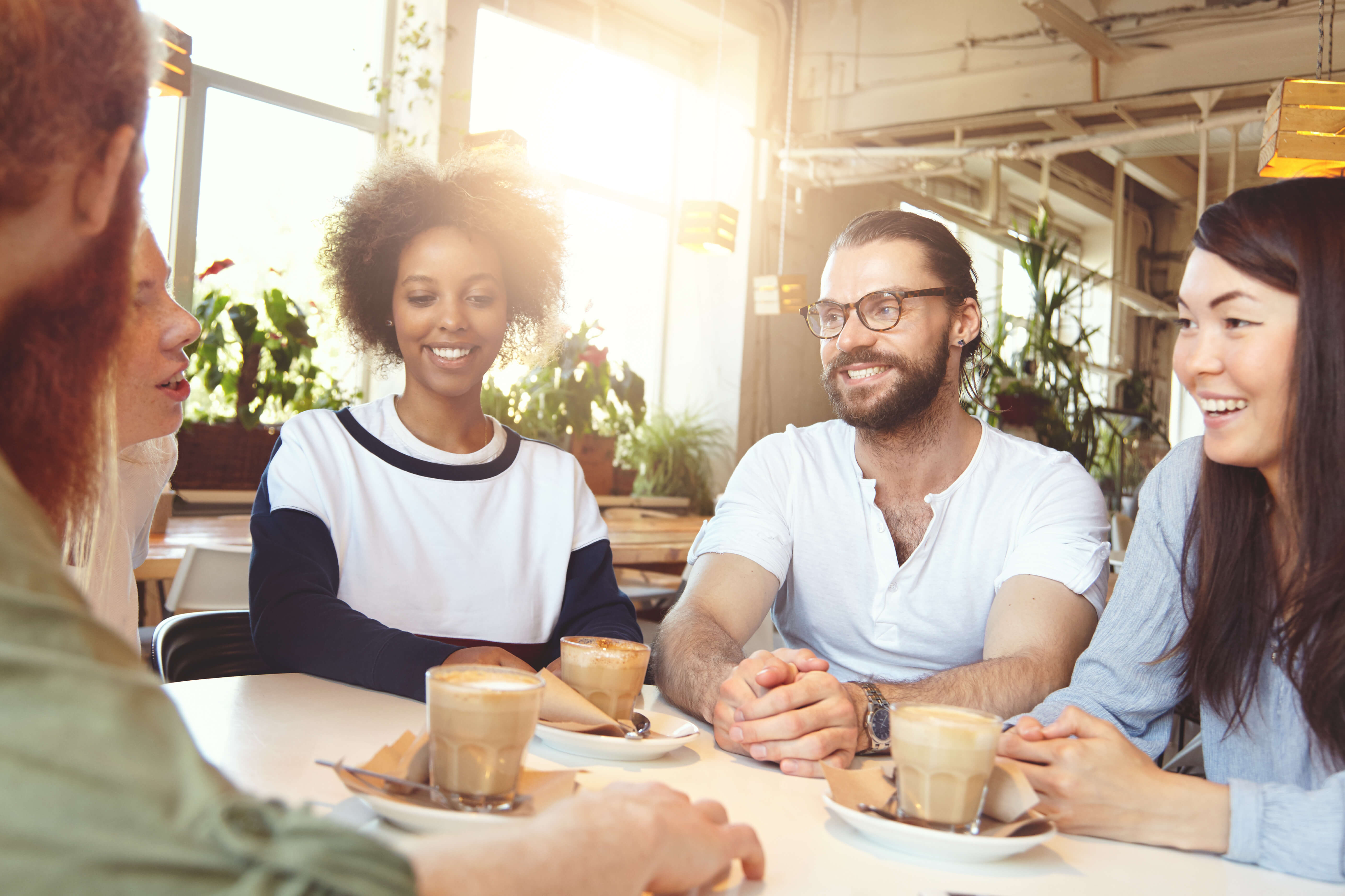 Group of happy young people of diverse nations and ethnicities sitting at table of coworking space for developing vision innovation and business solutions while planning their startup project