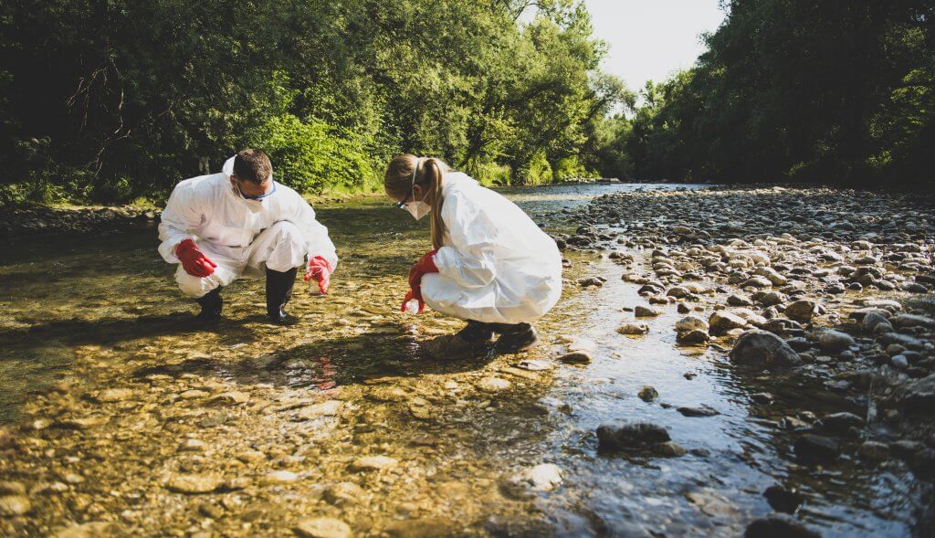 Image of two forensic scientists taking water samples in a contaminated river.